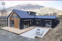 a black house with a wooden deck and a mountain in the background